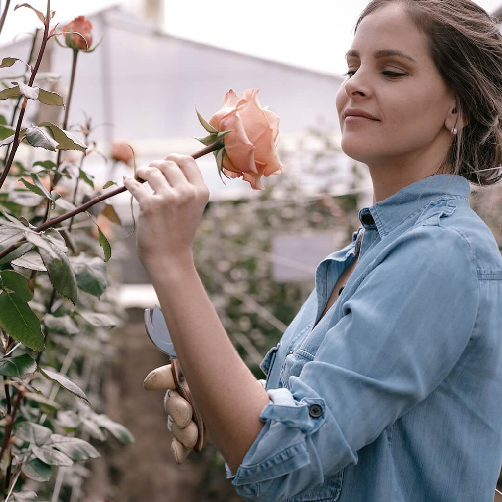 A woman holding and smelling a rose on a farm